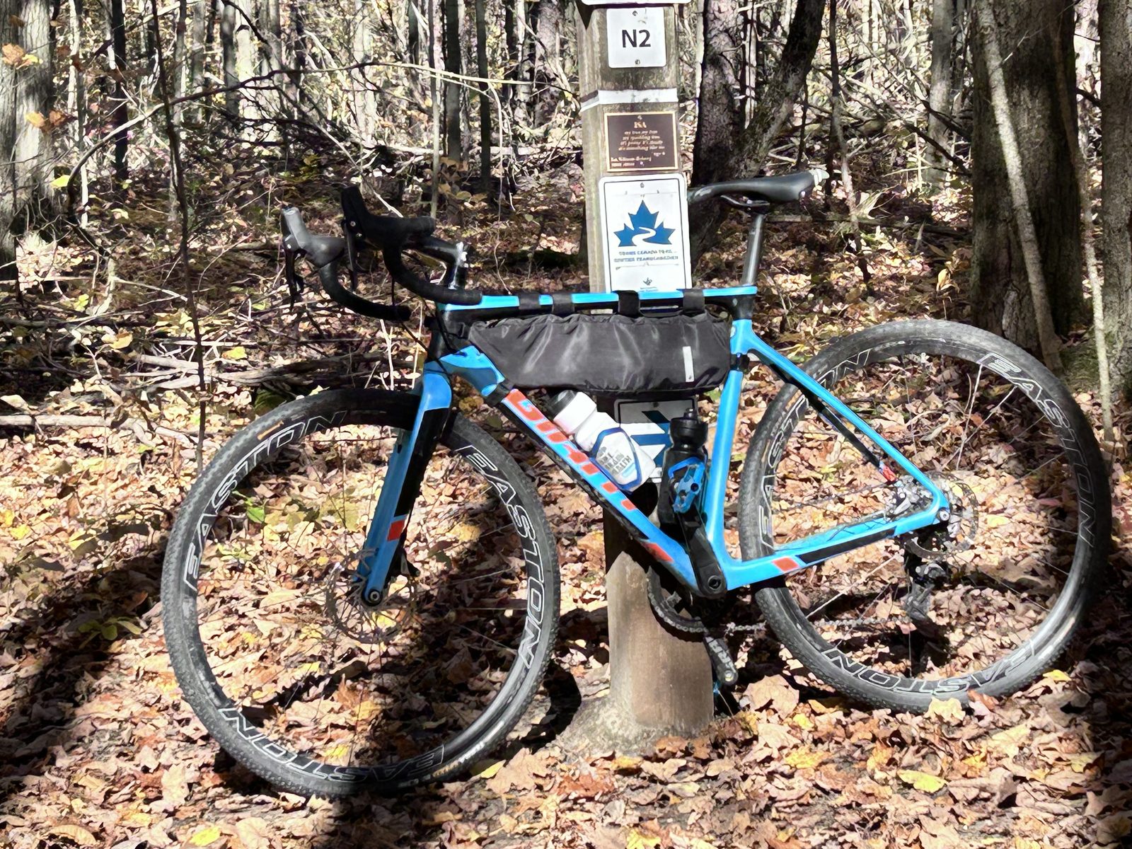 A blue gravel bike leaning against a wooden trail post marked N2 in a leafy forest