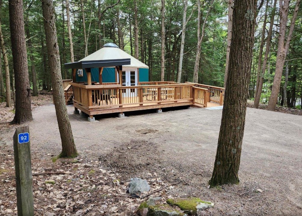 Yurt 92 at Silent Lake's Granite Ridge campground: a green-walled yurt with French doors on a large wooden deck, in a hemlock and pine forest, with the site post in the foreground.
